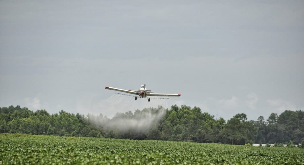 Ein Flugzeug spritzt Pestizide über ein Landwirtschaftsfeld.
