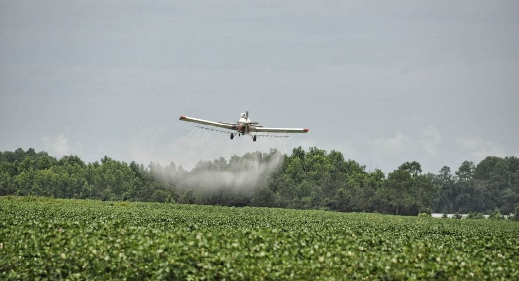 Ein Flugzeug spritzt Pestizide über ein Landwirtschaftsfeld.